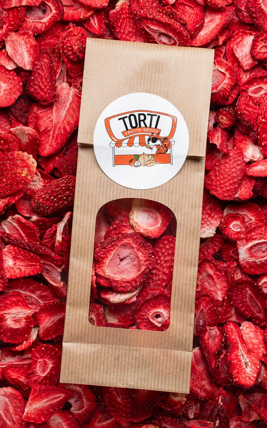 Busta kraft con finestra trasparente di fragole liofilizzate Torti Frutta Secca, adagiata su un letto di fette di fragole disidratate rosse — frutta liofilizzata premium da acquistare online